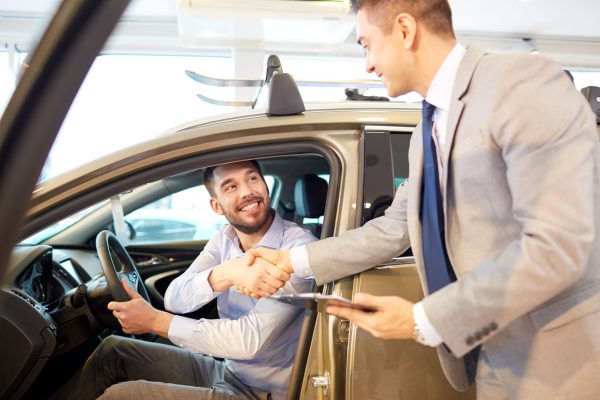 auto business, car sale, consumerism, gesture and people concept - happy man with car dealer making deal and shaking hands in auto show or salon
